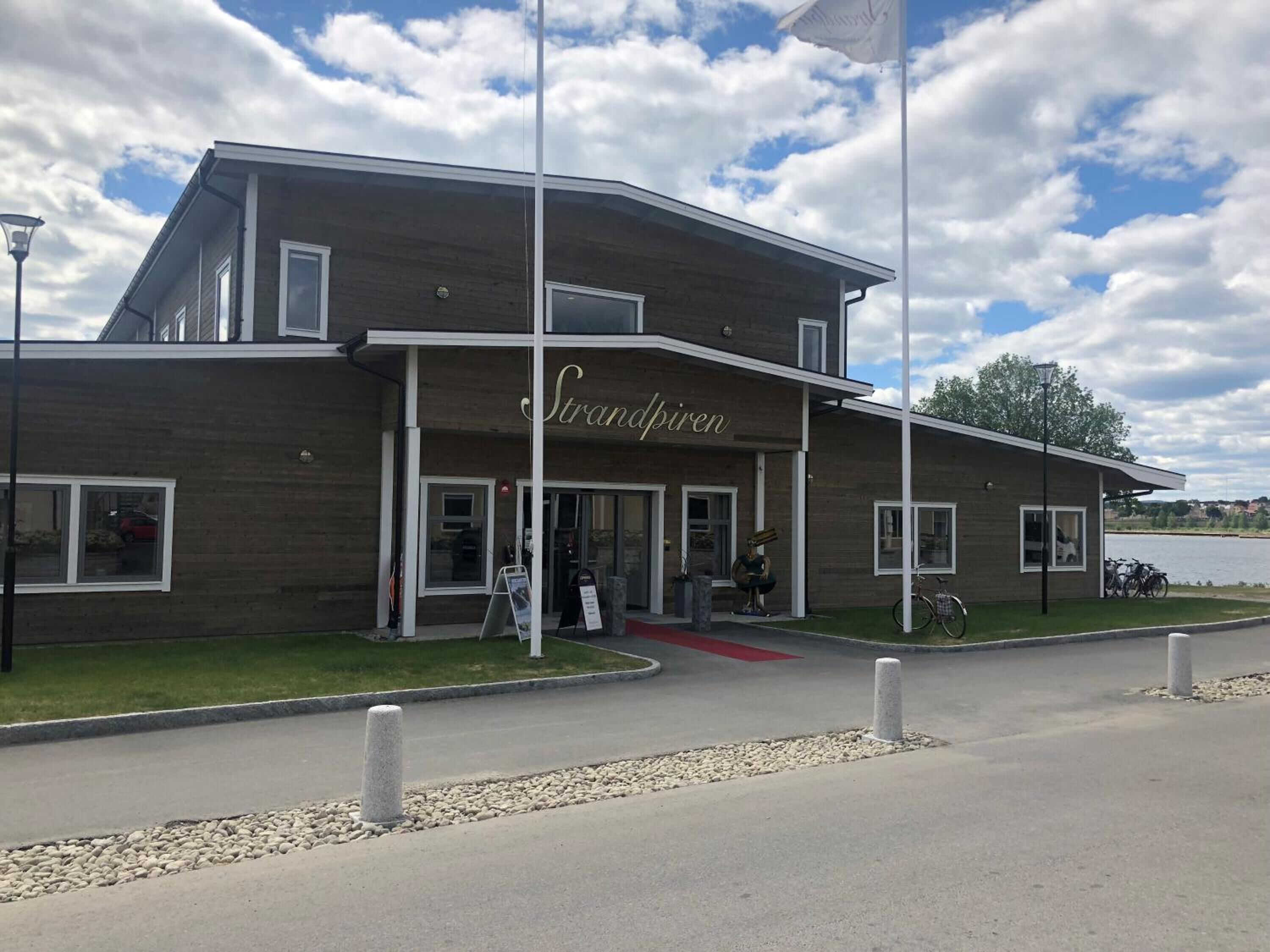 A modern building with a sign reading "Strandpiren." It features a flat roof, large windows, and a paved entrance area.