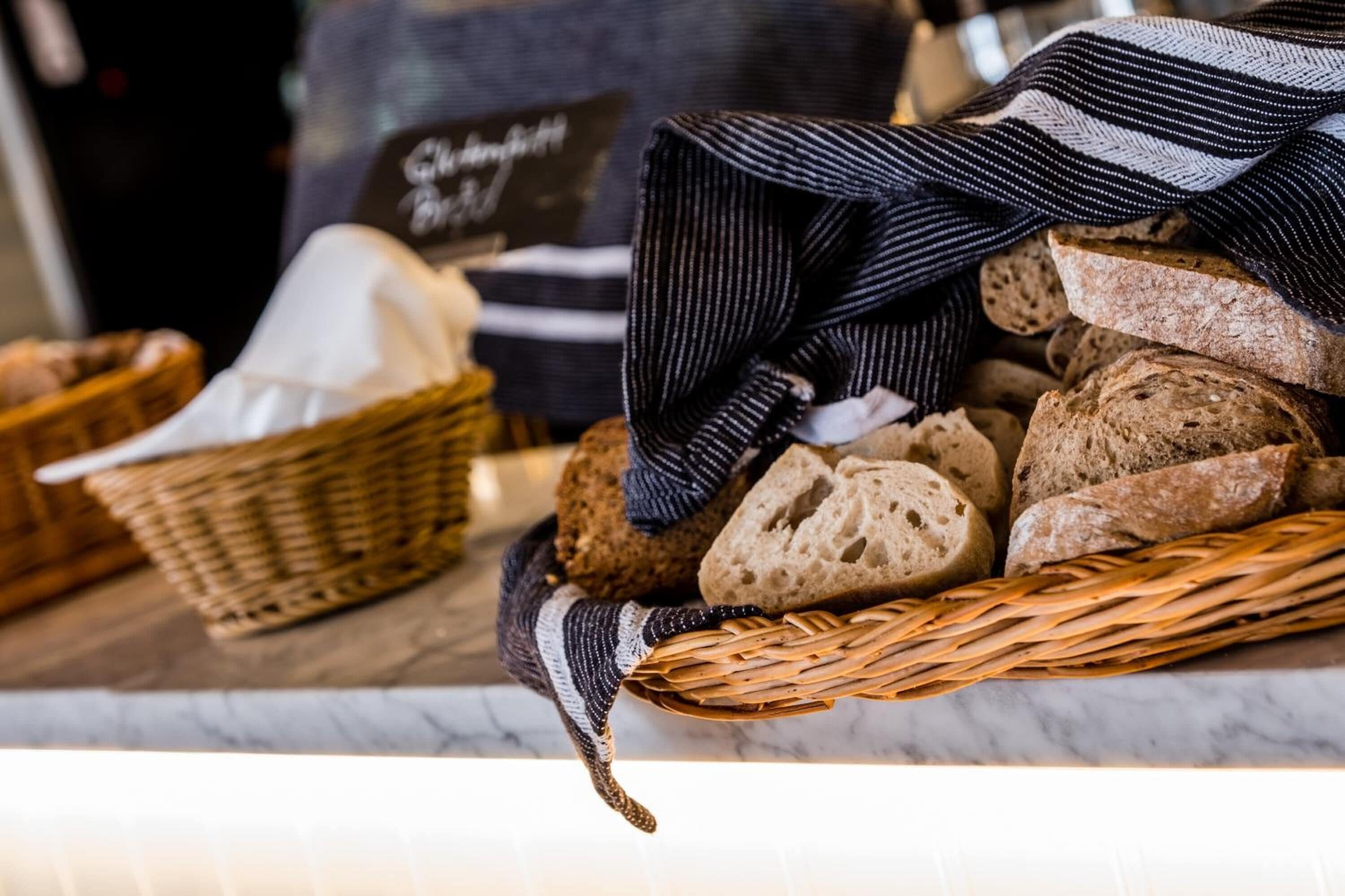 A basket of various breads and a woven basket with a striped cloth on a marble countertop.