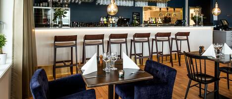 A restaurant with a bar area, multiple seating options including bar stools and tables, and a variety of hanging light fixtures.