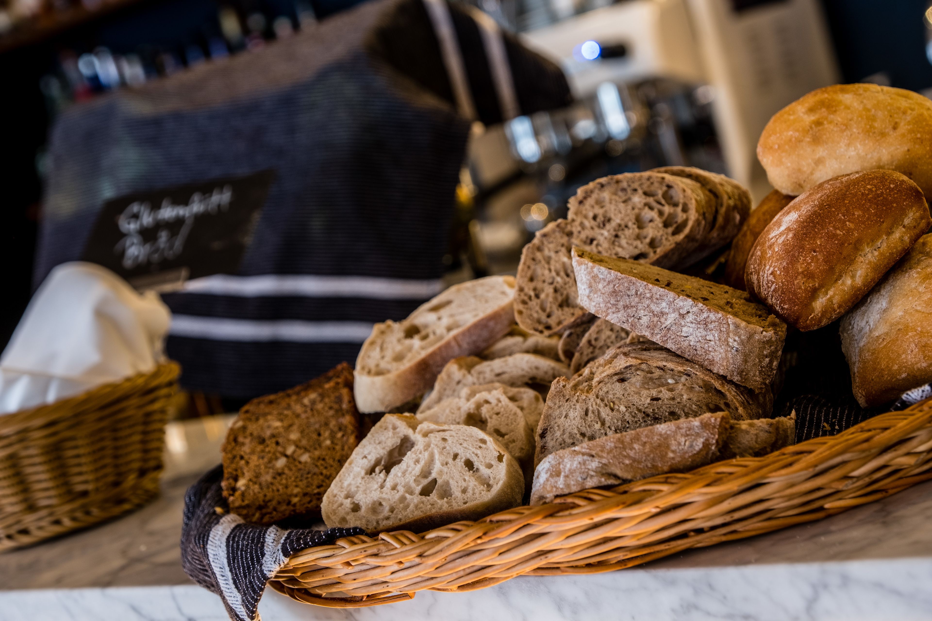 A basket of various breads on a marble surface.