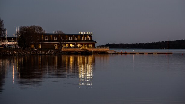 Un hotel con un llamativo letrero que dice 'HOTEL', ubicado junto a un lago tranquilo con un muelle que se adentra en el agua.