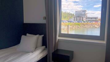 Ett sovrum med en säng, ett fönster och utsikt över en byggnad och parkerade bilar.