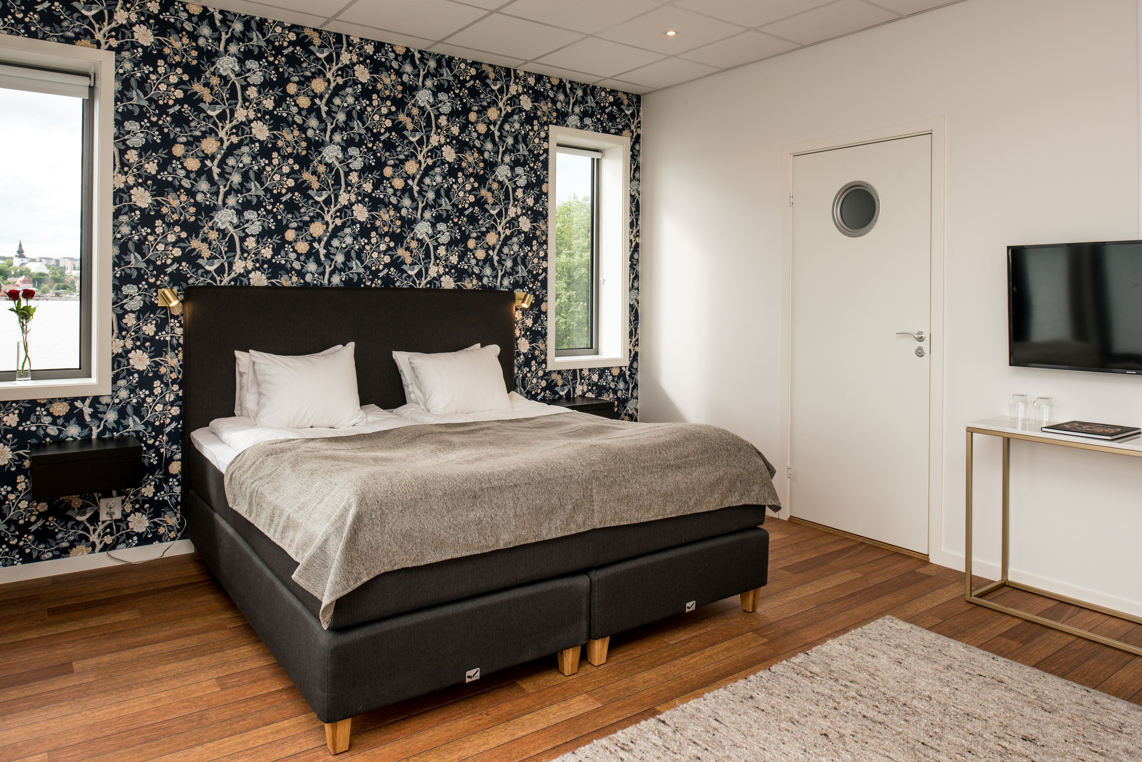 A bedroom with a large bed, a window, a TV, and a desk.