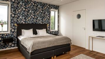 A bedroom with a large bed, a window, a TV, and a desk.