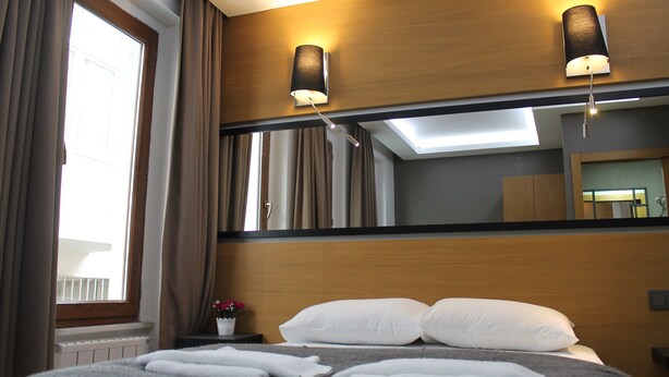 A hotel room with a large bed, two wall-mounted lamps, a window with curtains, and a mirror reflecting the room. - Xenia Hotel (Istanbul)