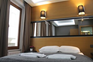 A hotel room with a large bed, two wall-mounted lamps, a window with curtains, and a mirror reflecting the room. - Xenia Hotel (Istanbul)