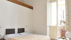 Une chambre moderne avec un lit, des poutres en bois, un balcon avec une balustrade et une porte blanche.