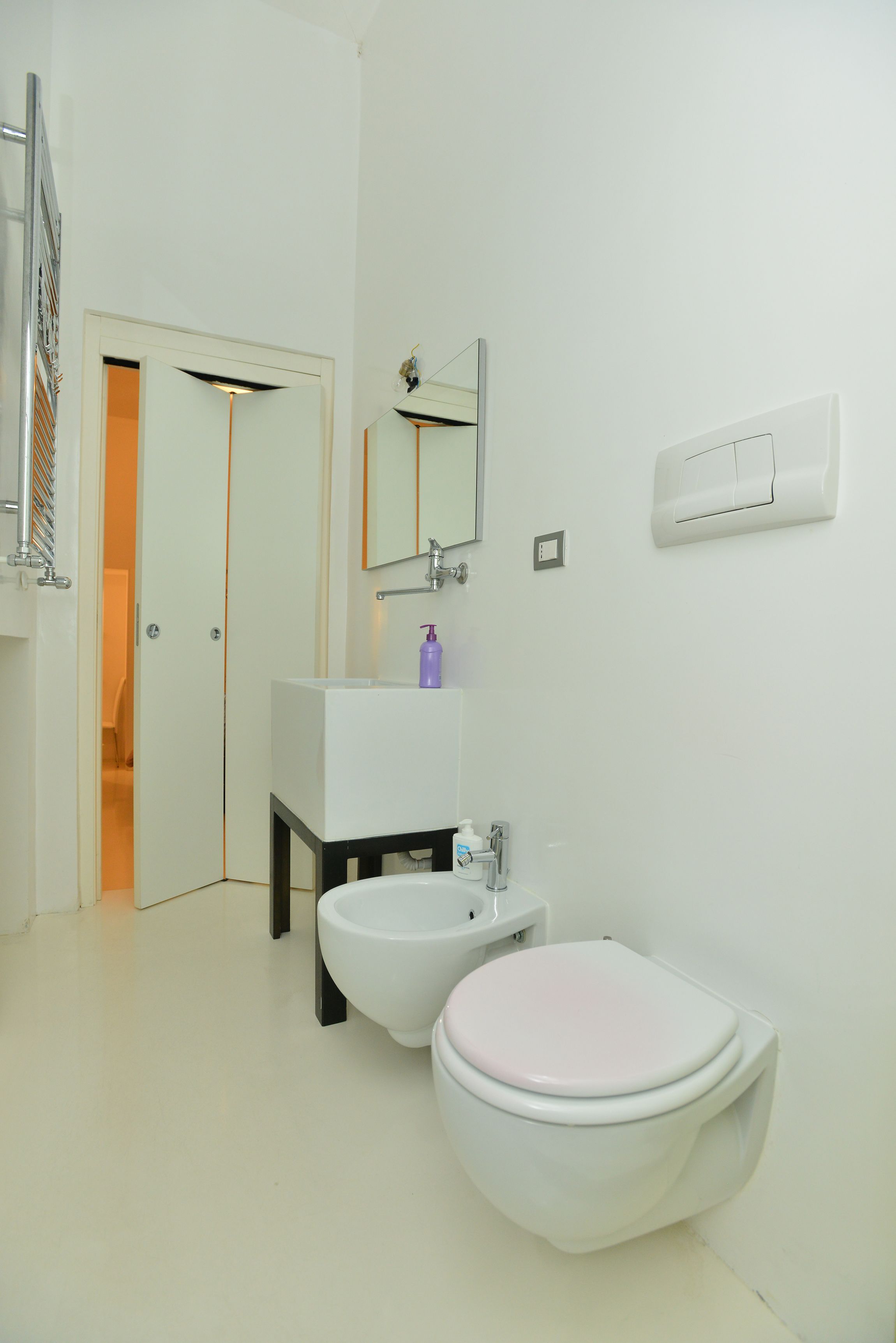 A modern bathroom with a white sink, bidet, toilet, and a mirror.
