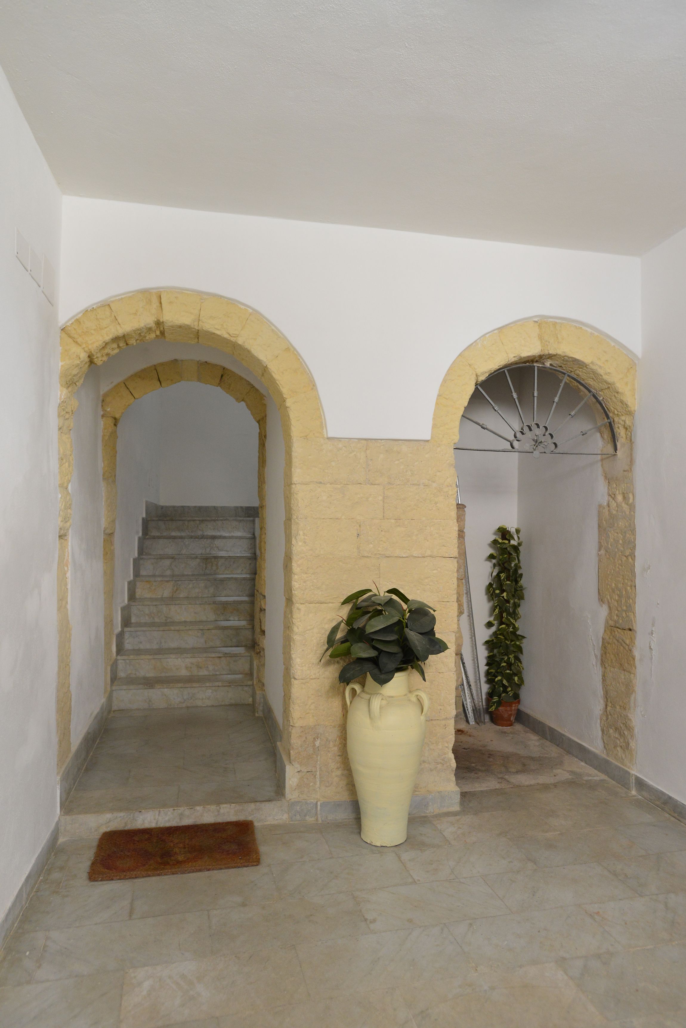 A staircase with stone steps leading to a landing, flanked by two arches with plants and a large vase.