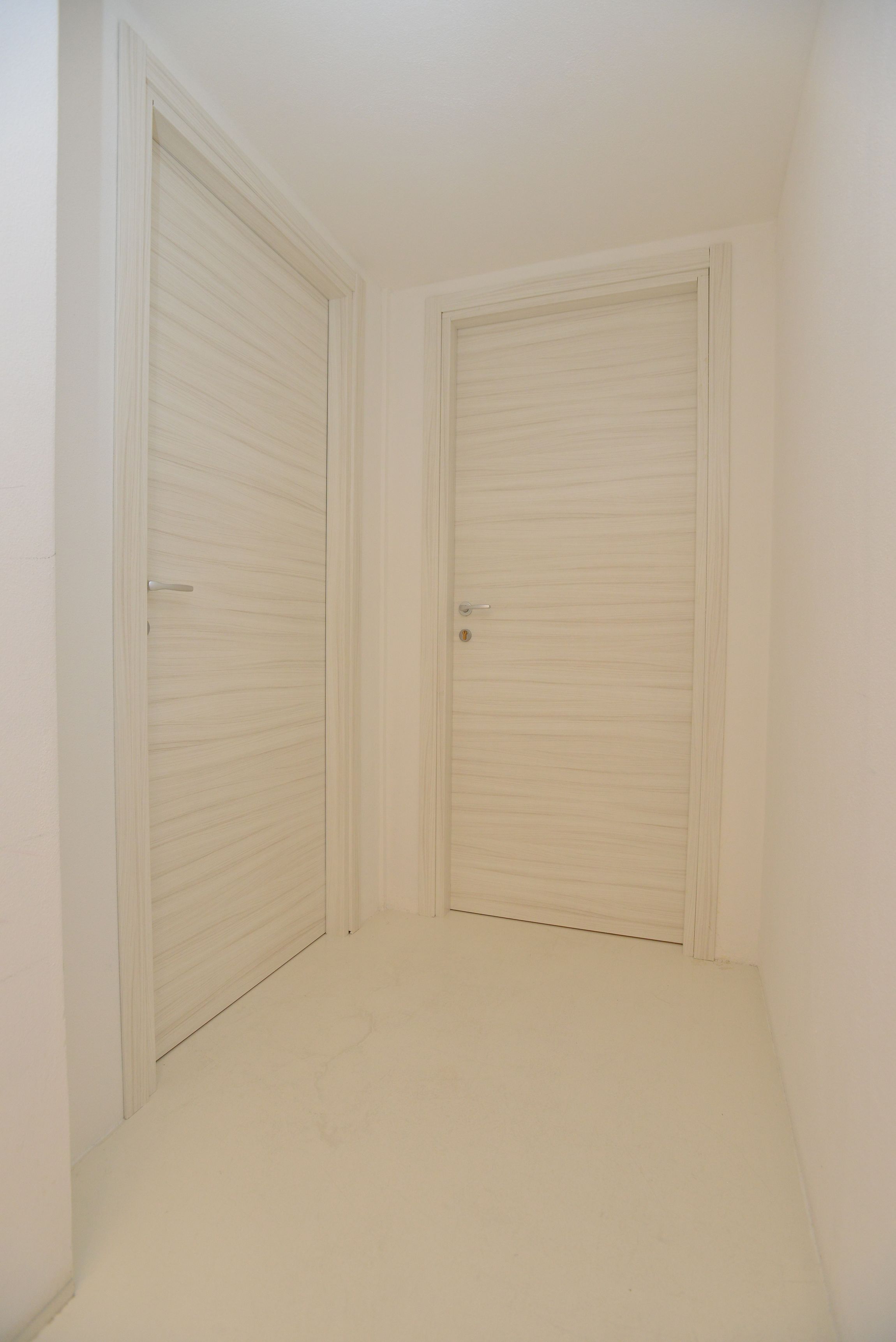 A small, empty room with two closed doors and a plain white floor.