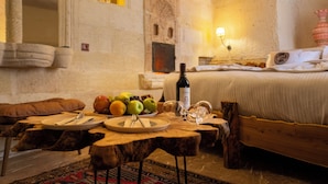 A rustic room with a bed, wooden table, and stone walls. - Urgup Evi Cave Hotel (Ürgüp)