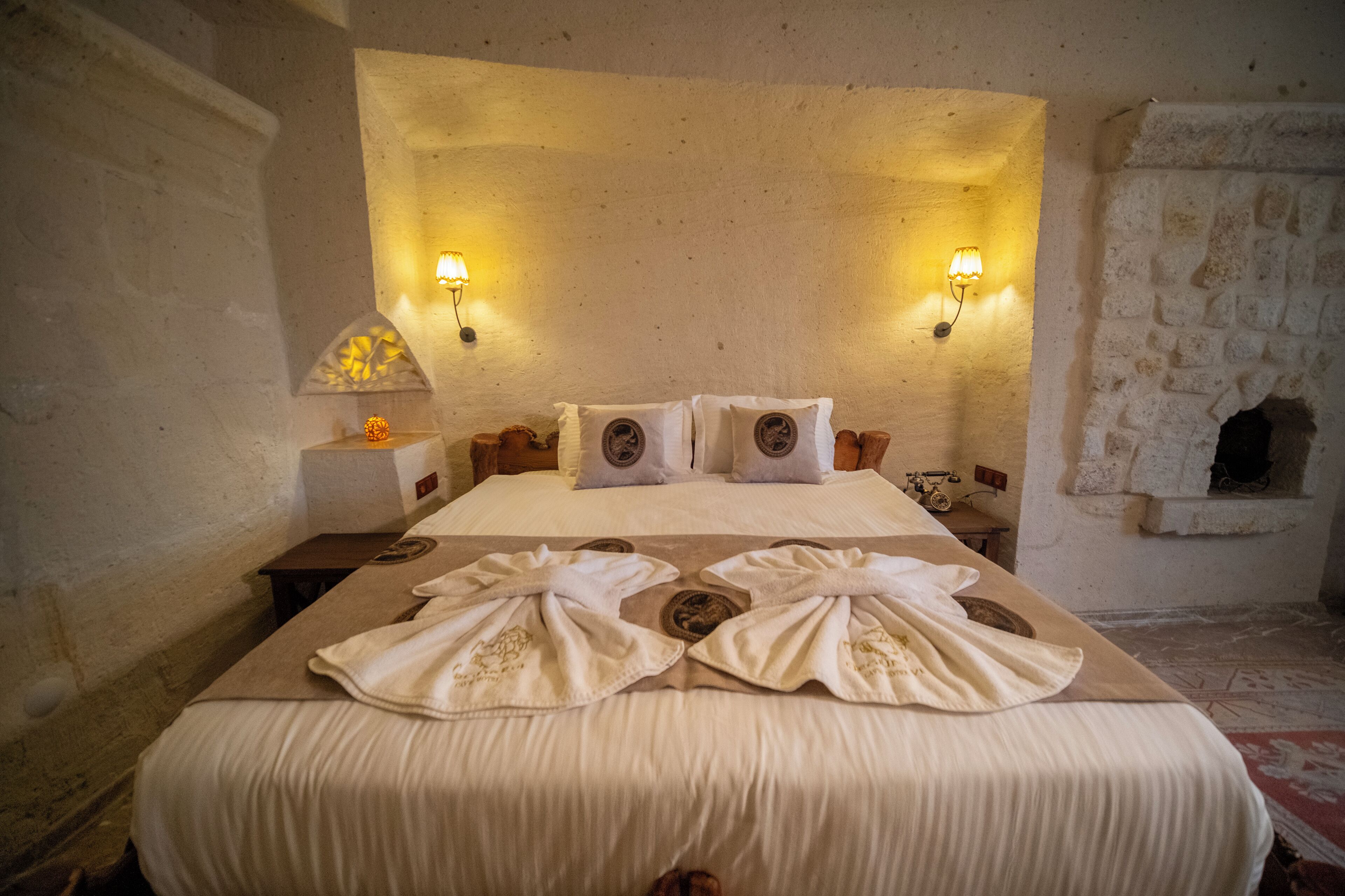 Une chambre d’hôtel avec un grand lit, deux lampes fixées au mur et un mur en pierre décoratif.