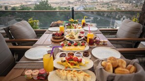 A table set for breakfast with various dishes and drinks, overlooking a scenic landscape. - Urgup Evi Cave Hotel (Ürgüp)