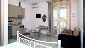 Un espacio habitable compacto con kitchenette, comedor y zona de estar con sofá y sillón.