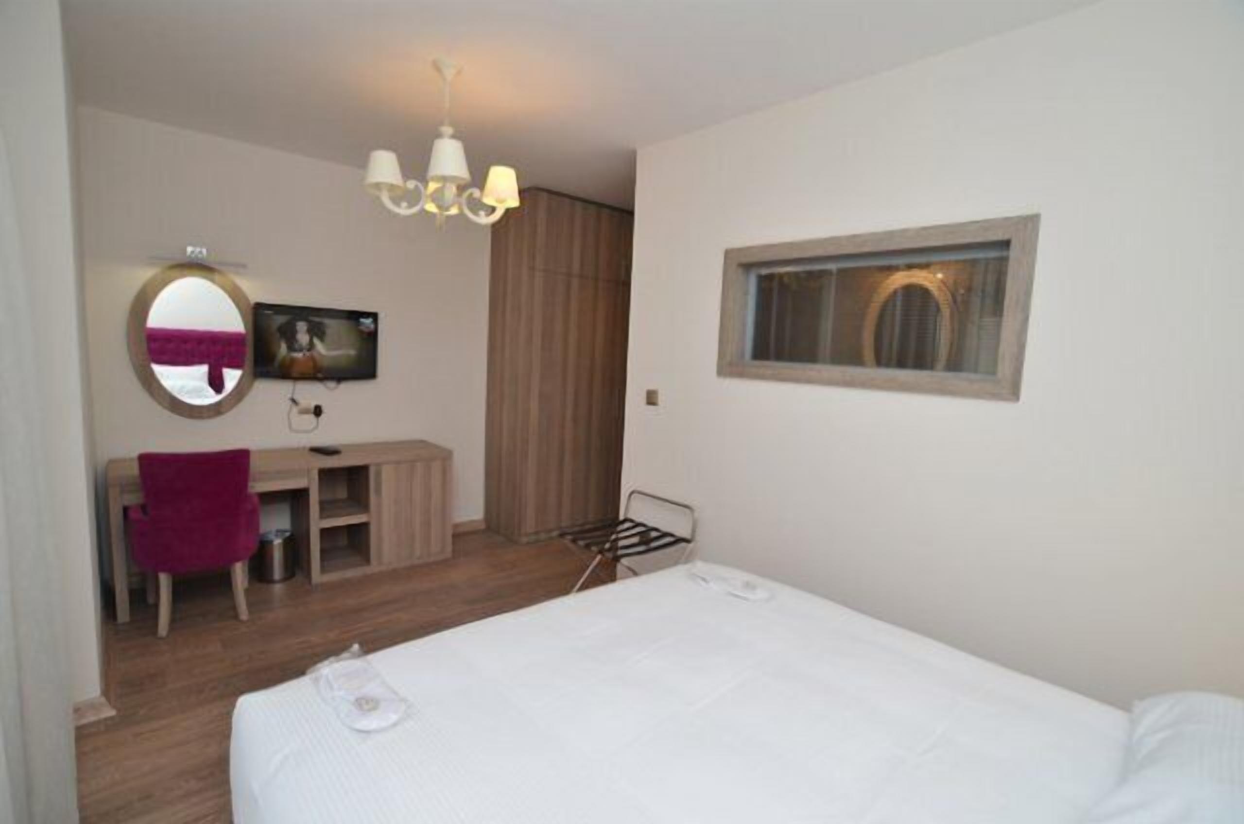 Habitación de hotel con cama, escritorio, silla, espejo, televisión y ventana.