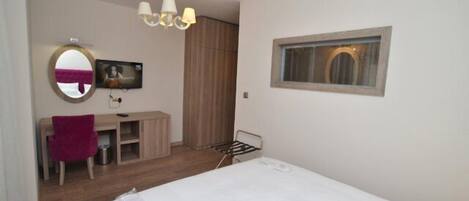 Habitación de hotel con cama, escritorio, silla, espejo, televisión y ventana.