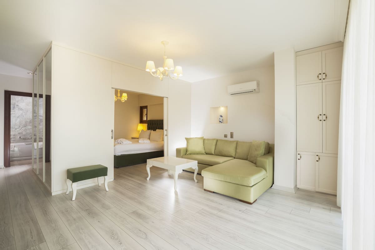 Habitación de hotel moderna con sofá verde, una mesa de centro blanca, un banco y un armario.