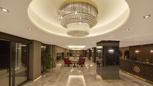 A spacious lobby with a large chandelier, a reception desk, and a seating area with red chairs.
