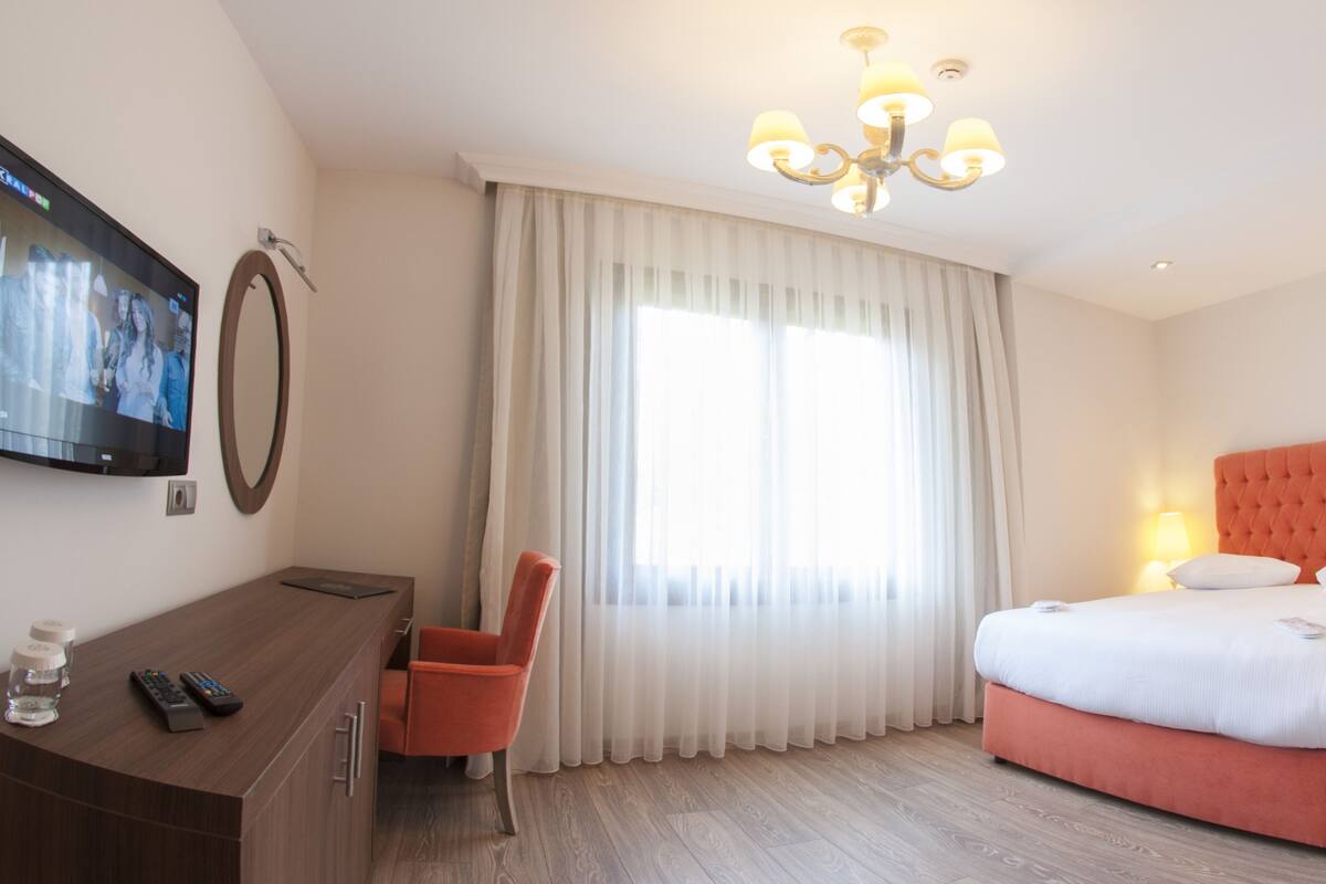 Una habitación de hotel con cama, escritorio, silla, televisor y ventana con cortinas.