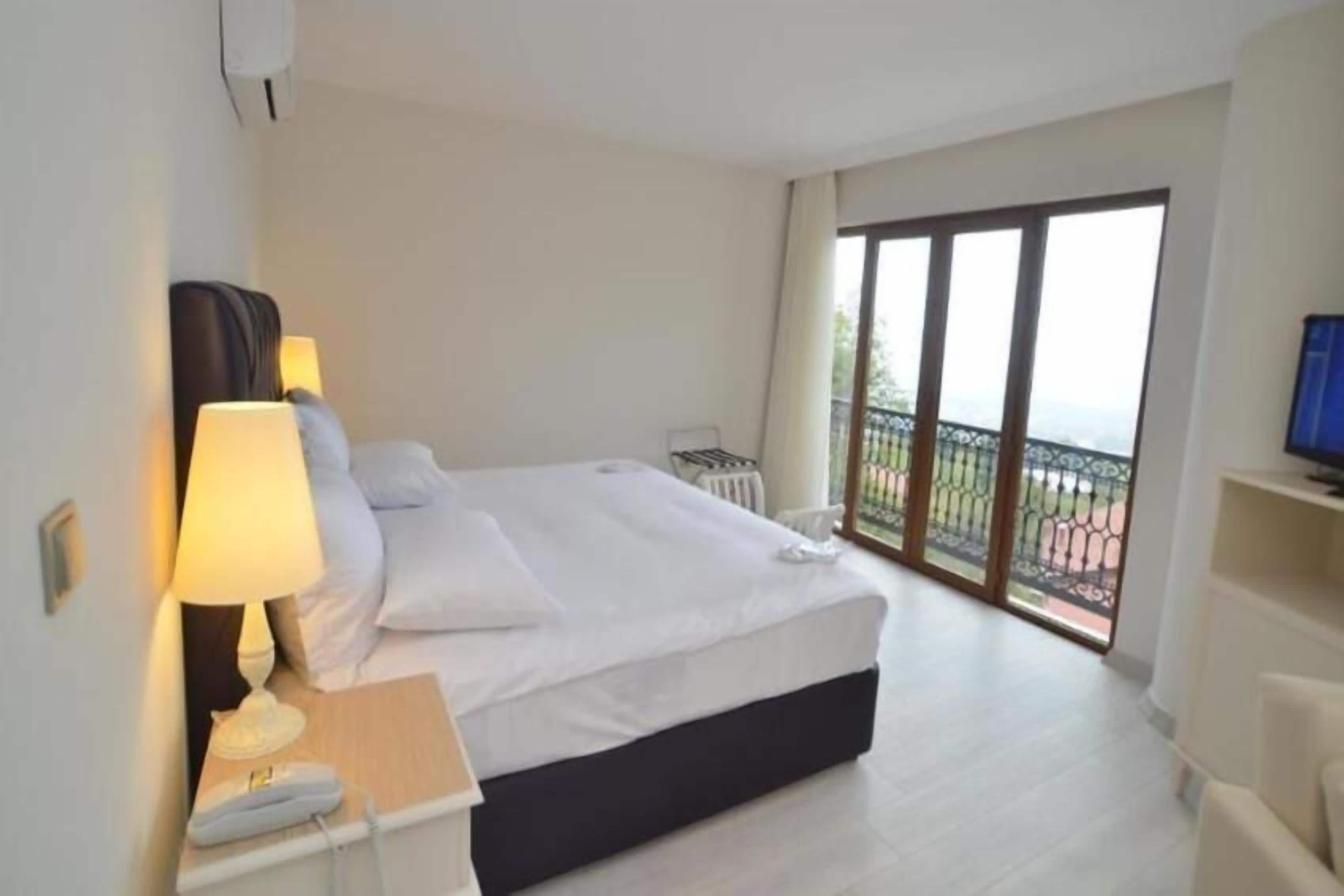 Een hotelkamer met een bed, bedlamp en uitzicht op een balkon.