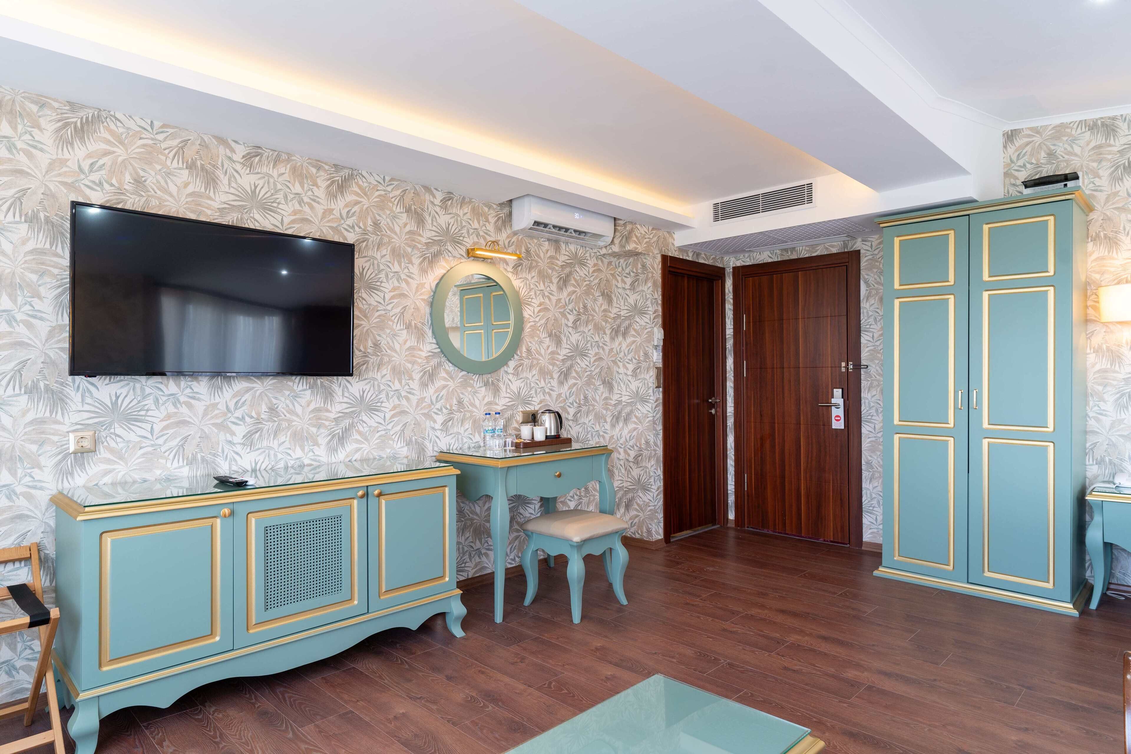 Une chambre dotée d’un téléviseur à écran plat, d’une coiffeuse avec un miroir, d’une porte en bois et d’une armoire de couleur turquoise.