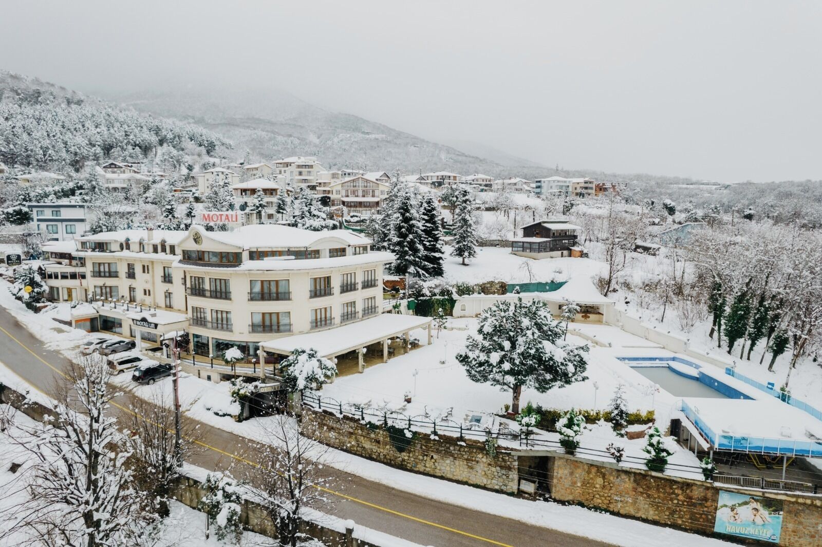 A snow-covered hotel with multiple buildings, a swimming pool, and a mountainous backdrop.