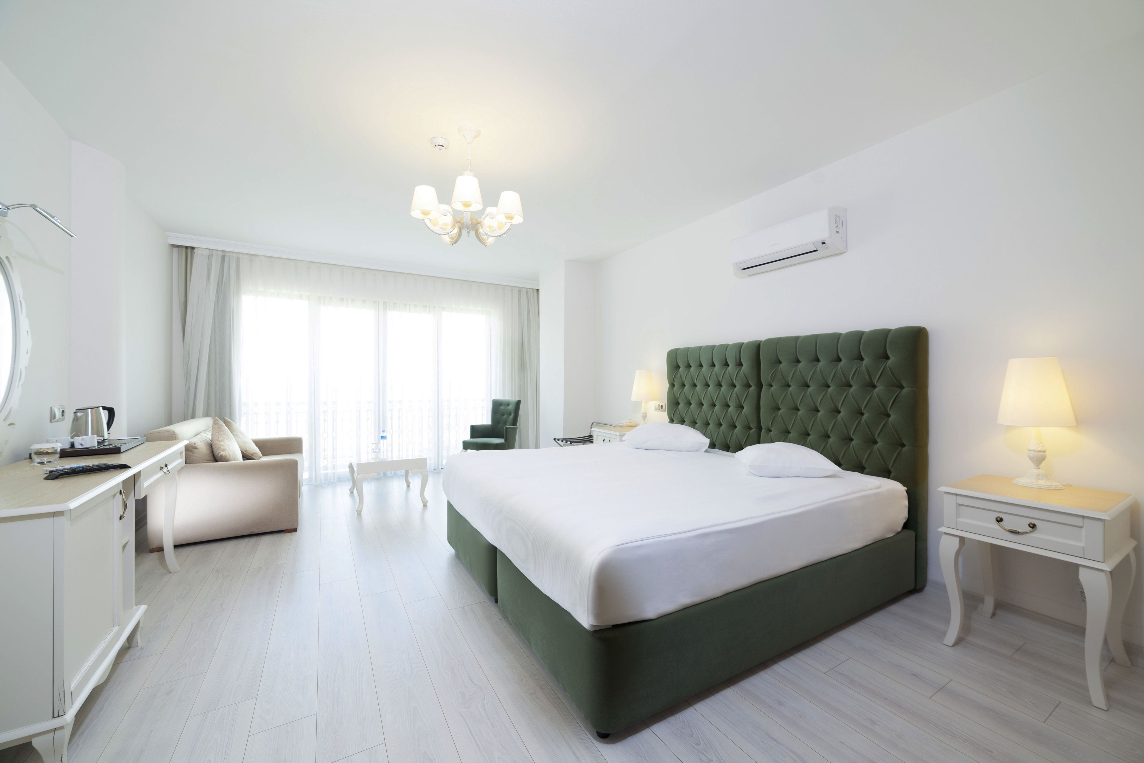 Habitación de hotel con una cama grande, un escritorio, una silla, una mesita de noche con lámpara y una ventana con cortinas.