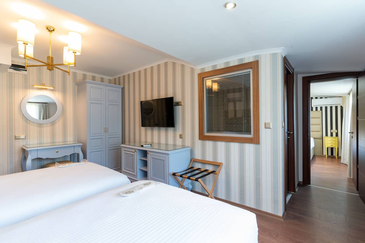 Habitación de hotel con una cama grande, tocador con espejo, televisión y ventana con persianas.