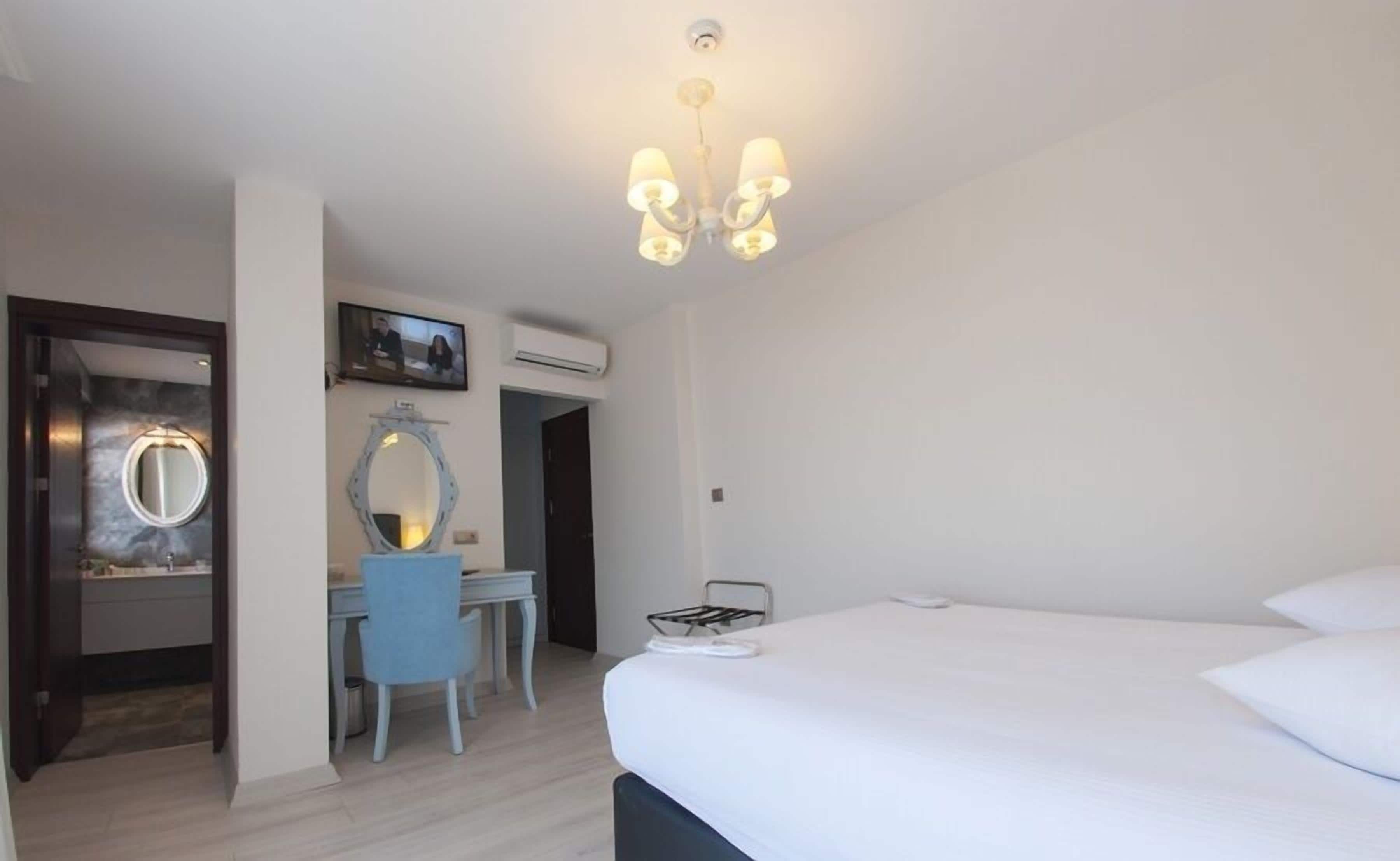 A hotel room with a bed, a desk with a chair, a large mirror, and a ceiling light fixture.
