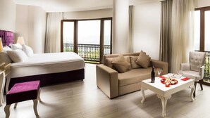 A hotel room with a bed, a sofa, a coffee table, and a chair. There is a balcony with a view.