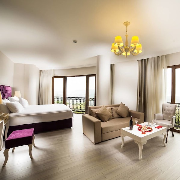 Une chambre d’hôtel avec un lit, un canapé, une table basse et une chaise. Elle dispose d’un balcon avec vue.
