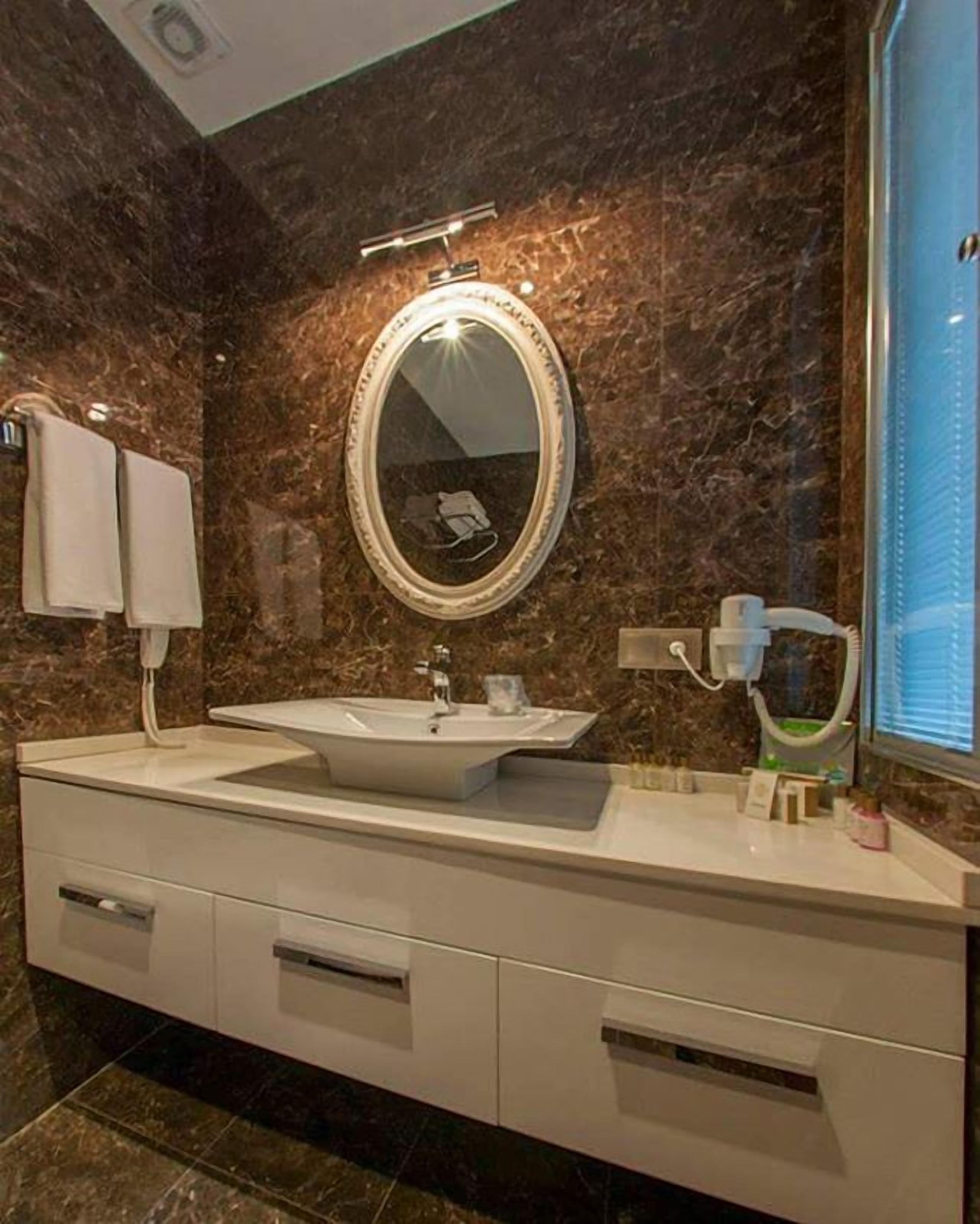 A modern bathroom with a large oval mirror, a white sink, and a towel rack.
