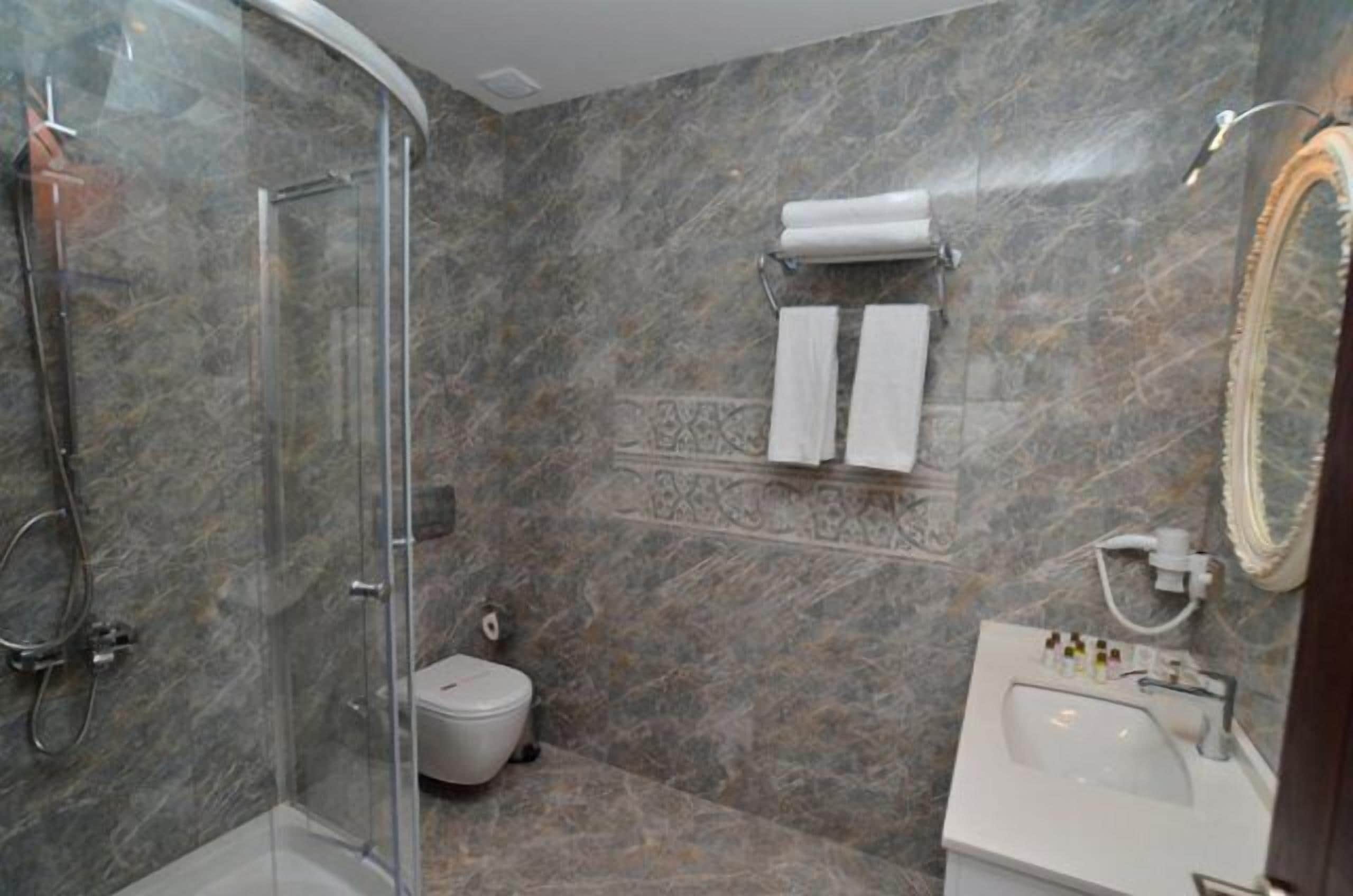 Ein Badezimmer mit einer Duschkabine, Toilette, Waschbecken mit Pflegeprodukten und einem Handtuchhalter.