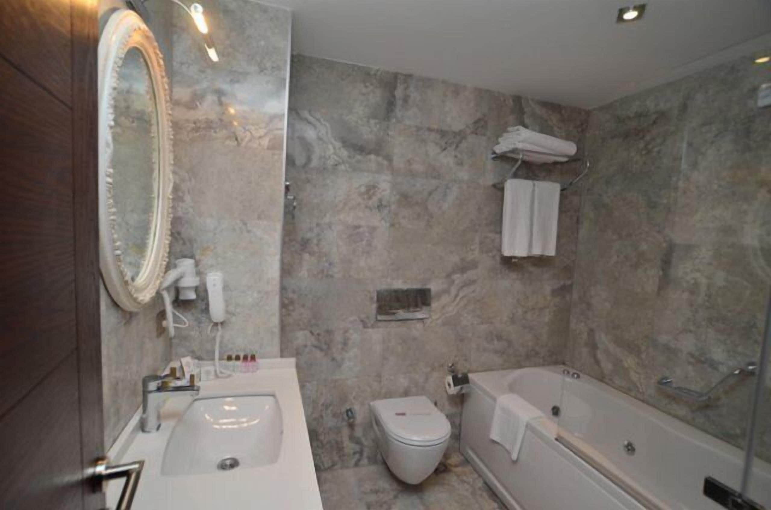Een badkamer met een marmeren wand, een wastafel, toilet en een bad.