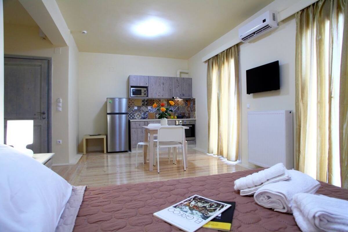 A compact hotel room with a bed, a small kitchenette, a TV, and a view of the outside.