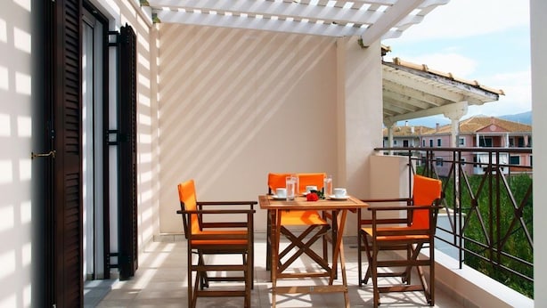 A balcony with a table and chairs, a pergola, and a view of buildings in the background. - Niriides (Lefkada)