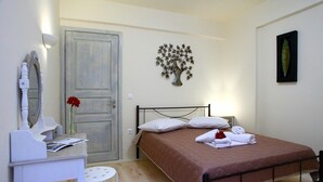 A bedroom with a bed, a desk, a chair, a mirror, a door, and a wall decoration. - Niriides (Lefkada)