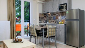 A modern kitchen with a stainless steel refrigerator, a microwave, and a patterned backsplash. There is a dining area with a table and chairs, and a view of the outdoors through a sliding glass door. - Niriides (Lefkada)