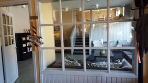 A room with a large window, a bookshelf, a staircase, and a seating area with cushions. - Highway (Harnosand)