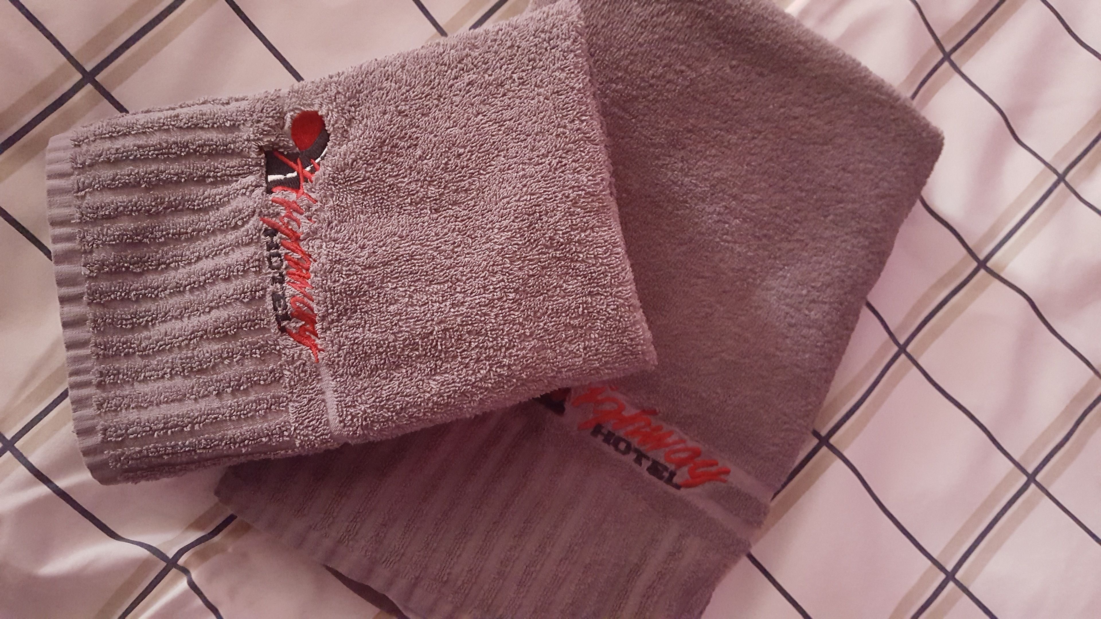 A bed with a white, grid-patterned bedspread and two folded towels with a textured surface and a red logo.