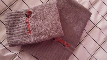 Uma cama com um edredom branco estampado em padrão quadriculado e duas toalhas dobradas com textura e logotipo vermelho.