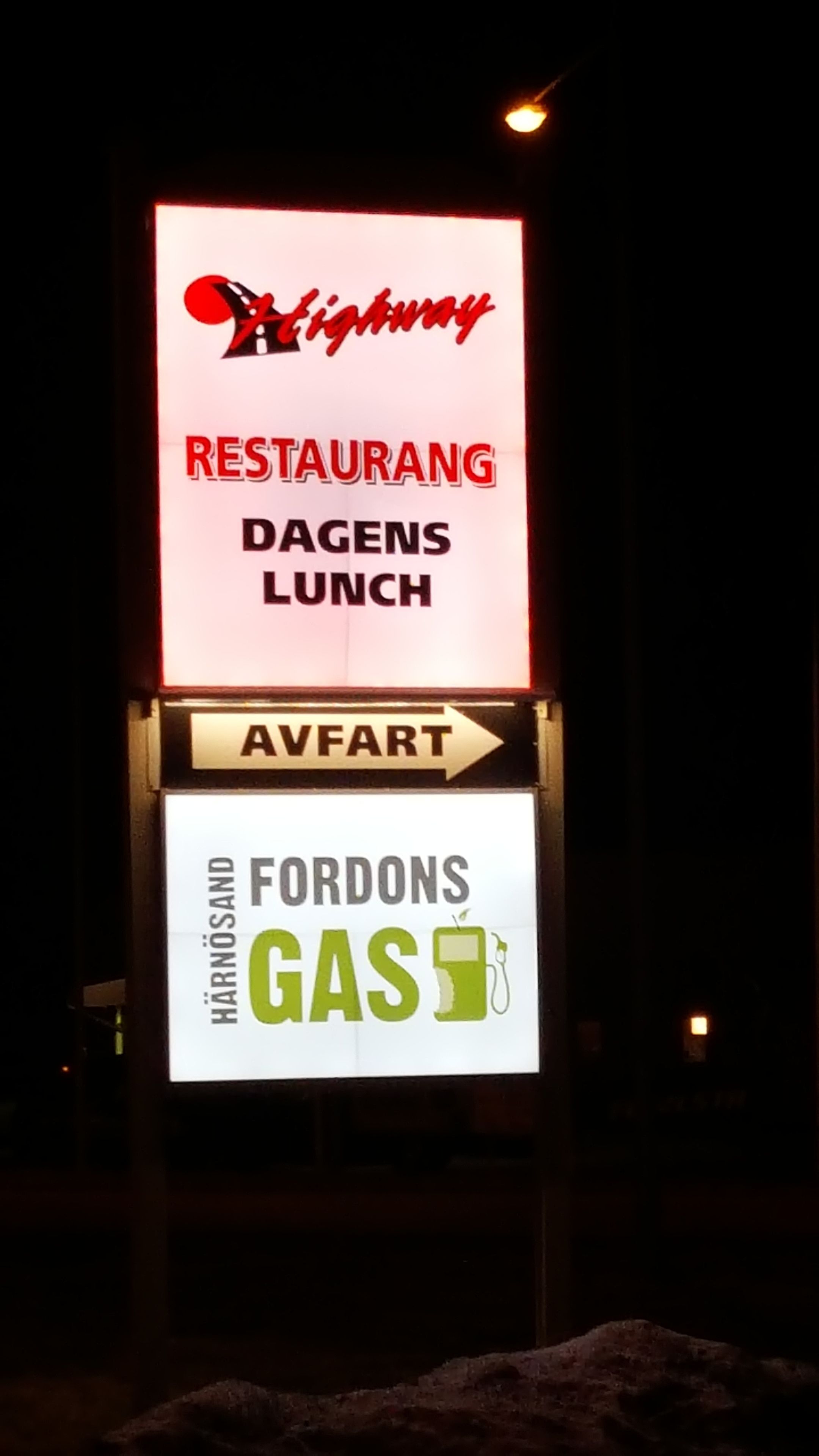 A nighttime signboard with the words "Highway RESTAURANG DAGENS LUNCH" and "AVFART" indicating directions.