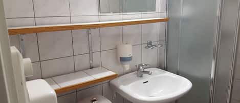 Un baño con un lavamanos blanco, dispensador de jabón, espejo y retrete.