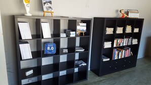 Two black shelving units with books and magazines, a small easel with a painting, and a vintage radio. - Highway (Harnosand)