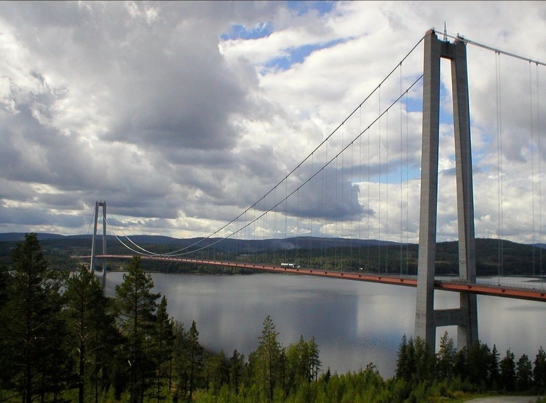 Un pont suspendu enjambant un lac paisible, avec des zones boisées au premier plan.