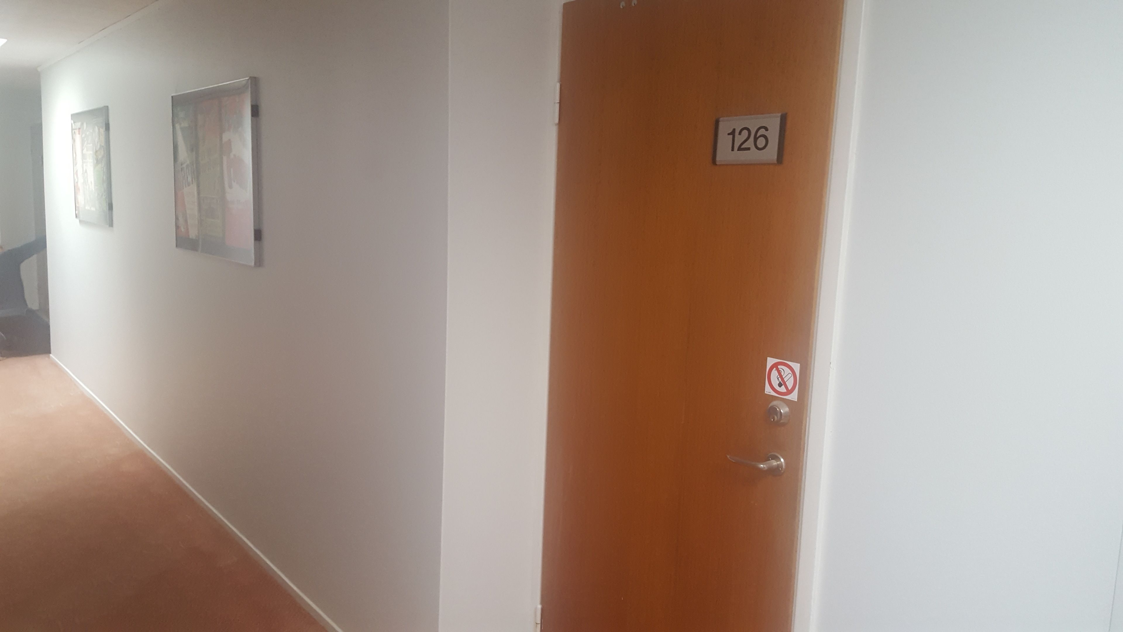 A hallway with a wooden door labeled 126, a no-smoking sign, and two framed pictures on the wall.