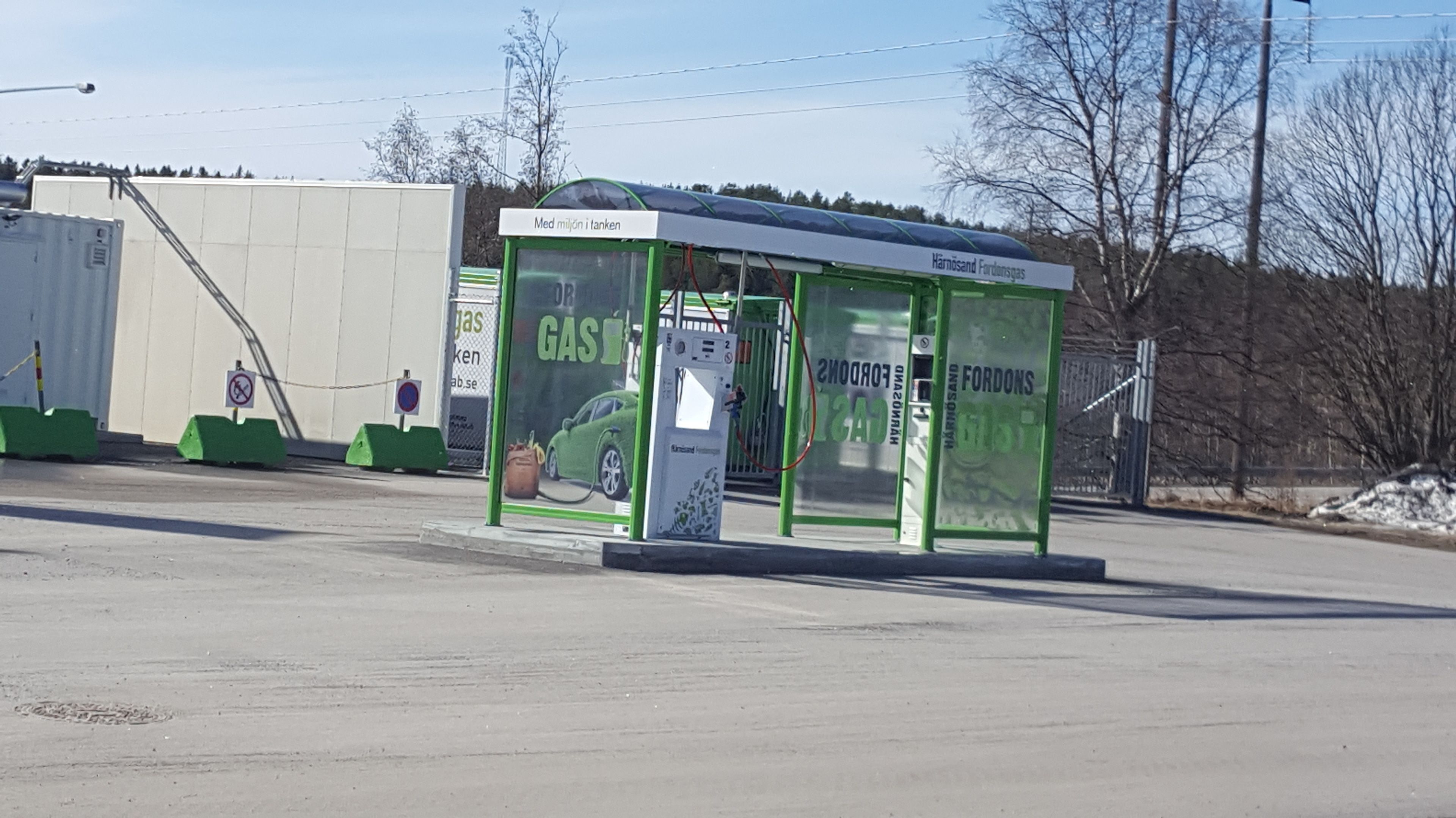En tankstation med et grønt markise og reklamer for benzin og Ford biler.