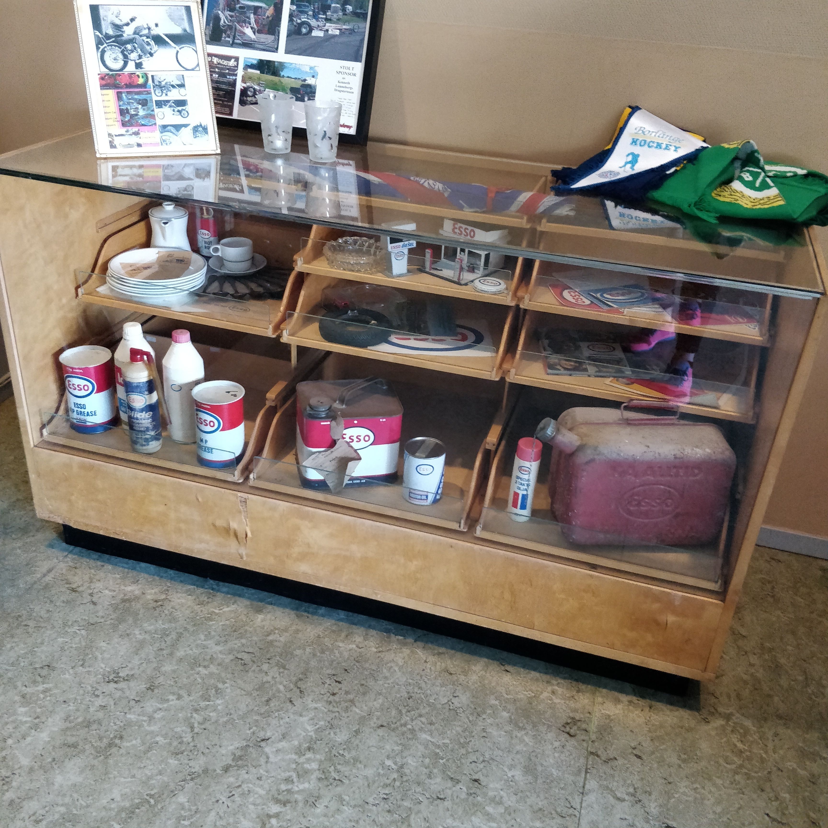 A display case with various items including cans of Esso, a large brick, and some sports memorabilia.