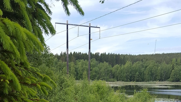 A picnic table and a fire pit in a natural setting with a lake and forest in the background. - Highway (Harnosand)