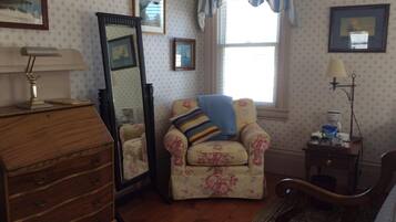 A room with a wooden dresser, a chair with a floral pattern, a mirror, and a window with blue curtains.